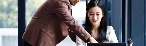 Man pointing at a laptop screen while discussing work with a colleague in a modern office