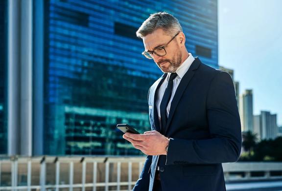 Confident businessman in a suit using a smartphone in a modern city business district.

