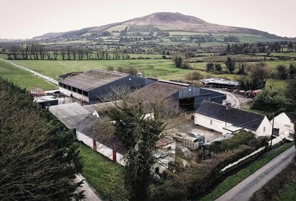 Aerial view of a rural farm complex surrounded by green fields and rolling hills, representing agricultural operations in the countryside