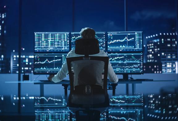 Man looking at 6 screens of financial data