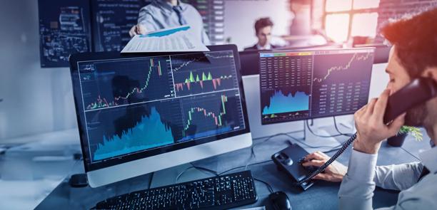 Um homem sentado em uma chamada telefônica olhando dados do mercado financeiro exibidos em várias telas
