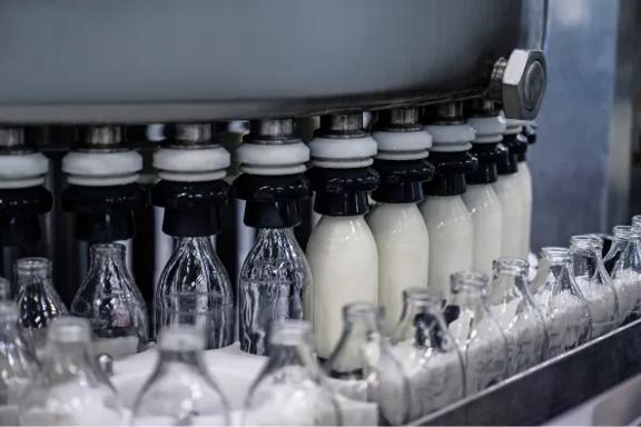 Garrafas de leite em movimento ao longo de uma linha de produção automatizada em uma instalação de processamento de laticínios