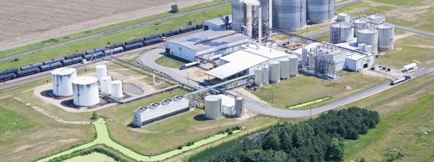 Aerial view of an industrial processing plant with storage tanks and rail access, representing energy or agricultural commodities infrastructure.