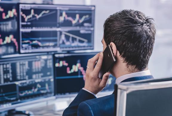 Profissional de negócios discutindo tendências de mercado ao telefone enquanto analisa gráficos financeiros em várias telas