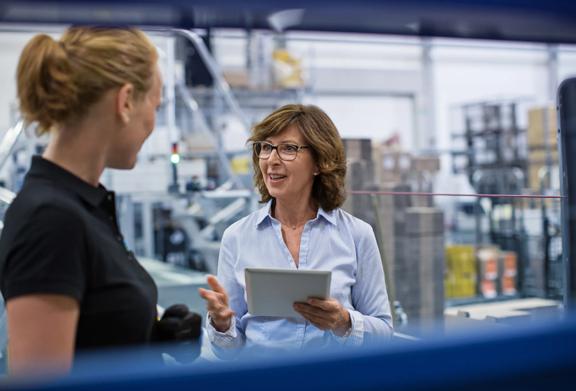 Two women discussing operations in a modern warehouse or manufacturing facility