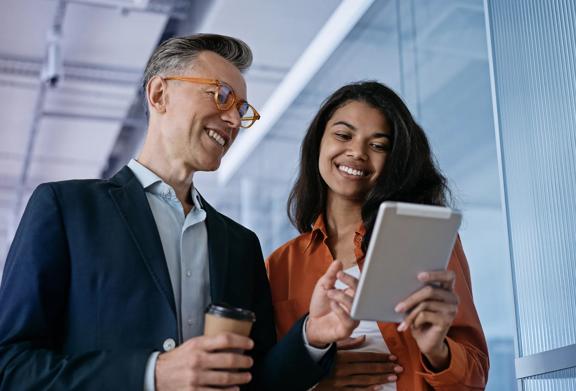 Two smiling professionals reviewing content on a digital tablet in a modern office setting