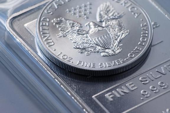 Close-up of a United States silver coin on a silver bullion bar showing fine silver purity.