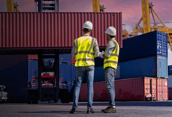 Workers overseeing shipping container loading at a port terminal during sunset