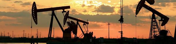 Multiple oil pumpjacks silhouetted against sunset sky, representing fossil fuel extraction