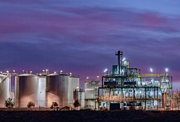Instalação industrial com tanques iluminados e estruturas de processamento no crepúsculo