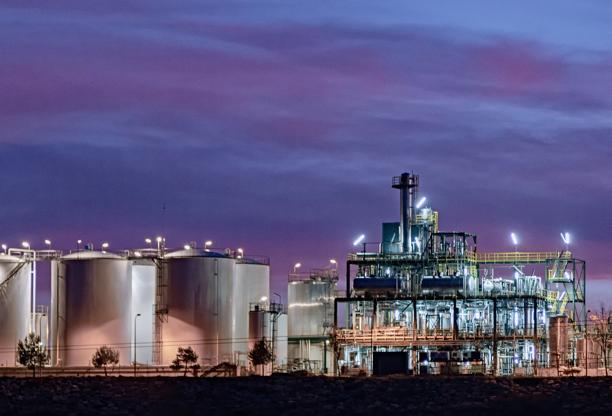 Instalação industrial com tanques iluminados e estruturas de processamento no crepúsculo