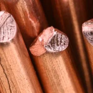 Close‑up of cut copper rods showing textured ends and smooth cylindrical surfaces under warm industrial lighting