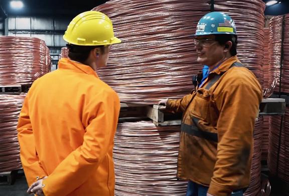 Two men in safety helmets standing in front of large copper reels