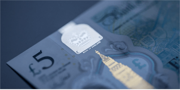Close up view of a Bank of England five pound banknote highlighting security features, currency design elements, and financial value representation.
