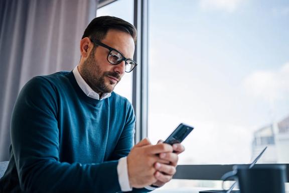 Person using a smartphone while seated at a table near a window.